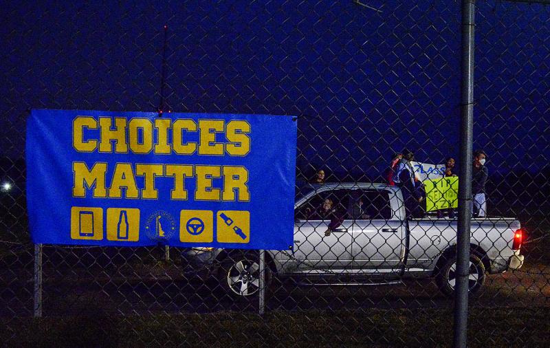 As cars drive by and honk, masked seniors show off a sign that says R.I.P Senior Class.